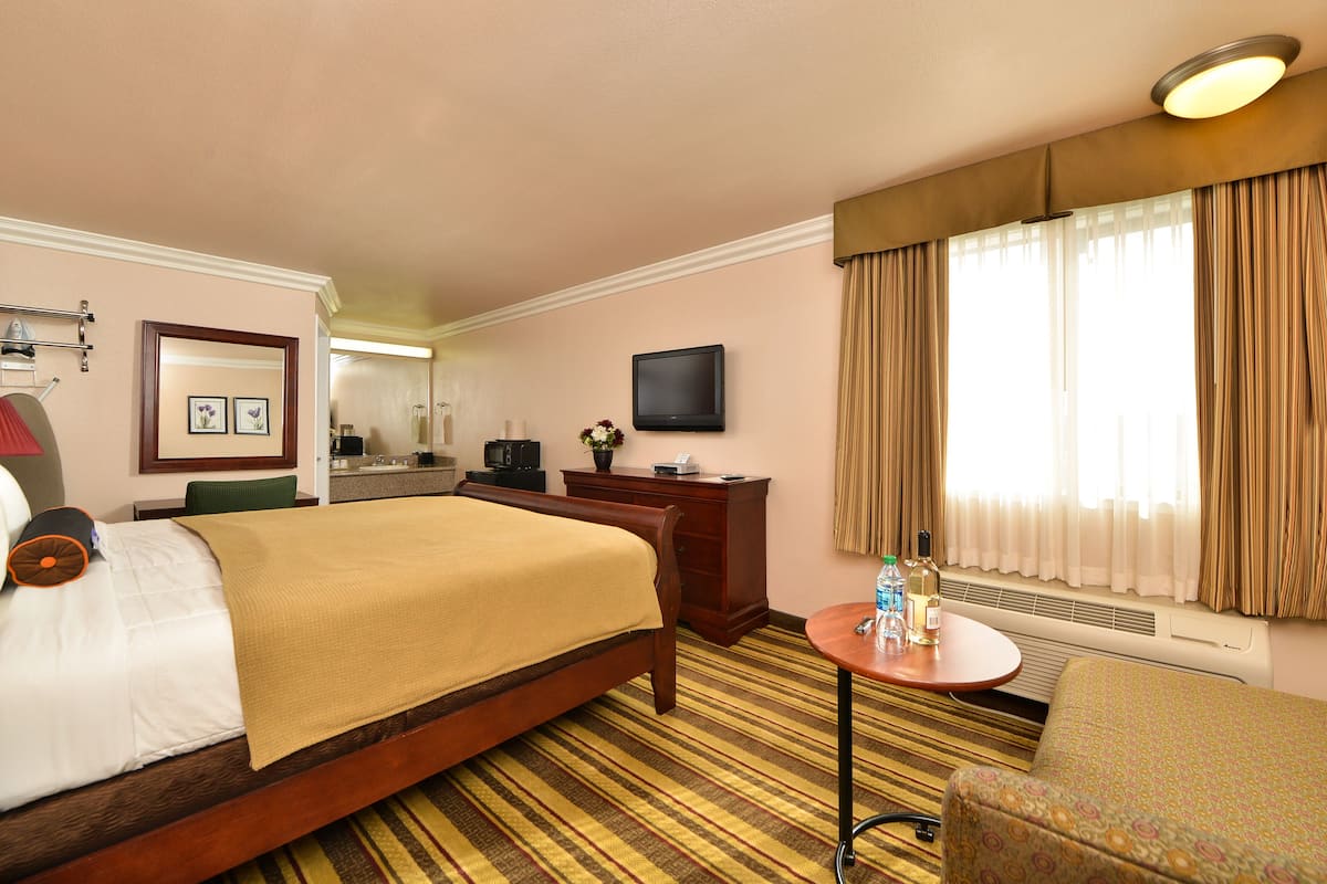 A hotel room with a bed, a desk, a chair, a television, and a window with curtains.