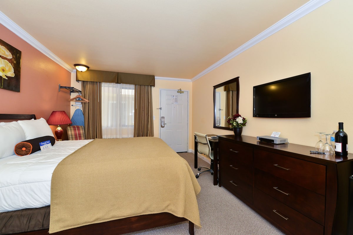 A hotel room with a bed, a desk, a dresser, a TV, and a door.