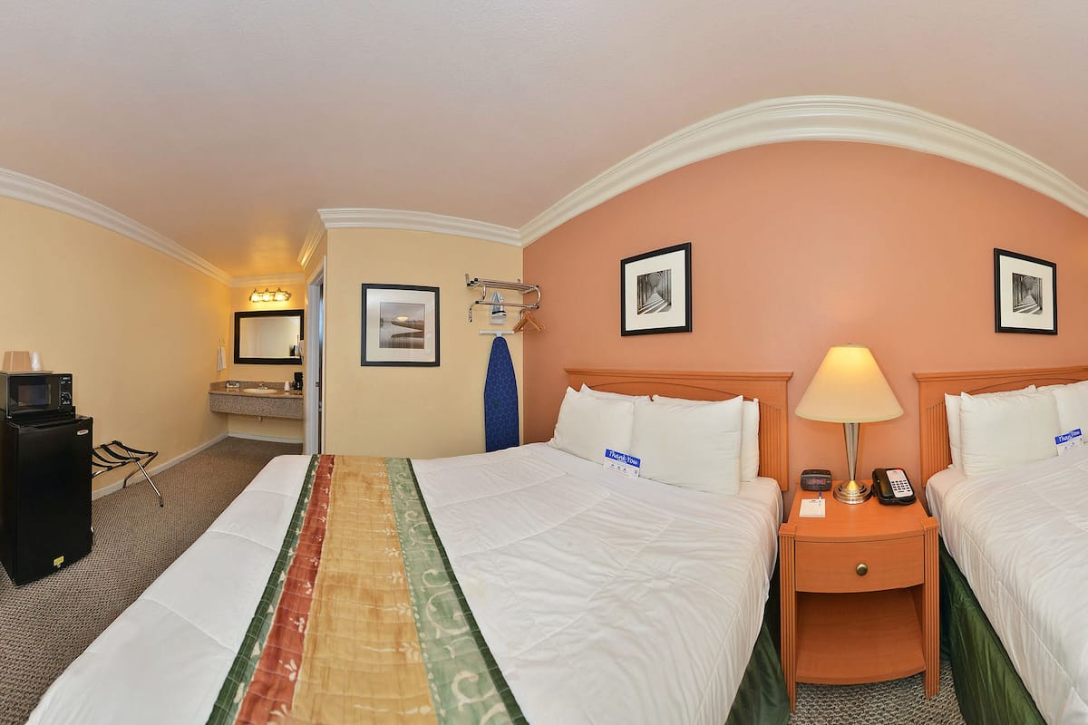 A hotel room with two beds, a desk, a TV, and a bathroom.