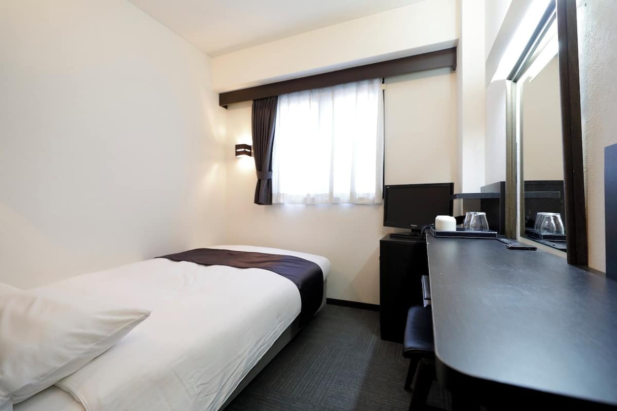 A hotel room with a single bed, a desk with a computer, and a window with curtains.