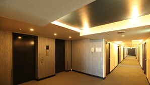 A hotel hallway with carpeted floors, wooden walls, and multiple doors, some with signs. - Tokyo Inn (Tokyo)
