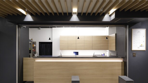 A modern reception area with a wooden counter, a digital display, and a seating bench. - Tokyo Inn (Tokyo)