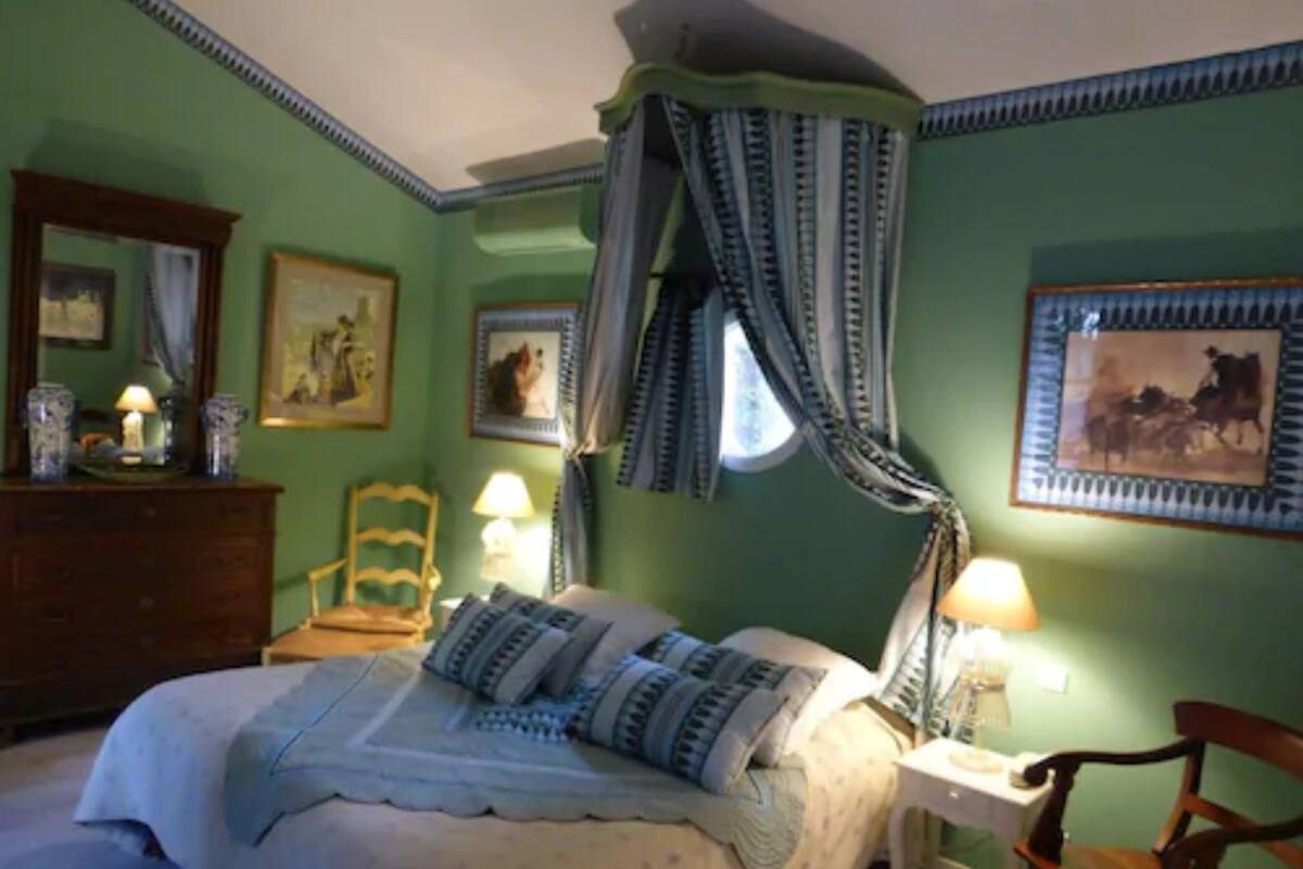 Une chambre à coucher avec un lit, une chaise, une commode et une fenêtre avec des rideaux.