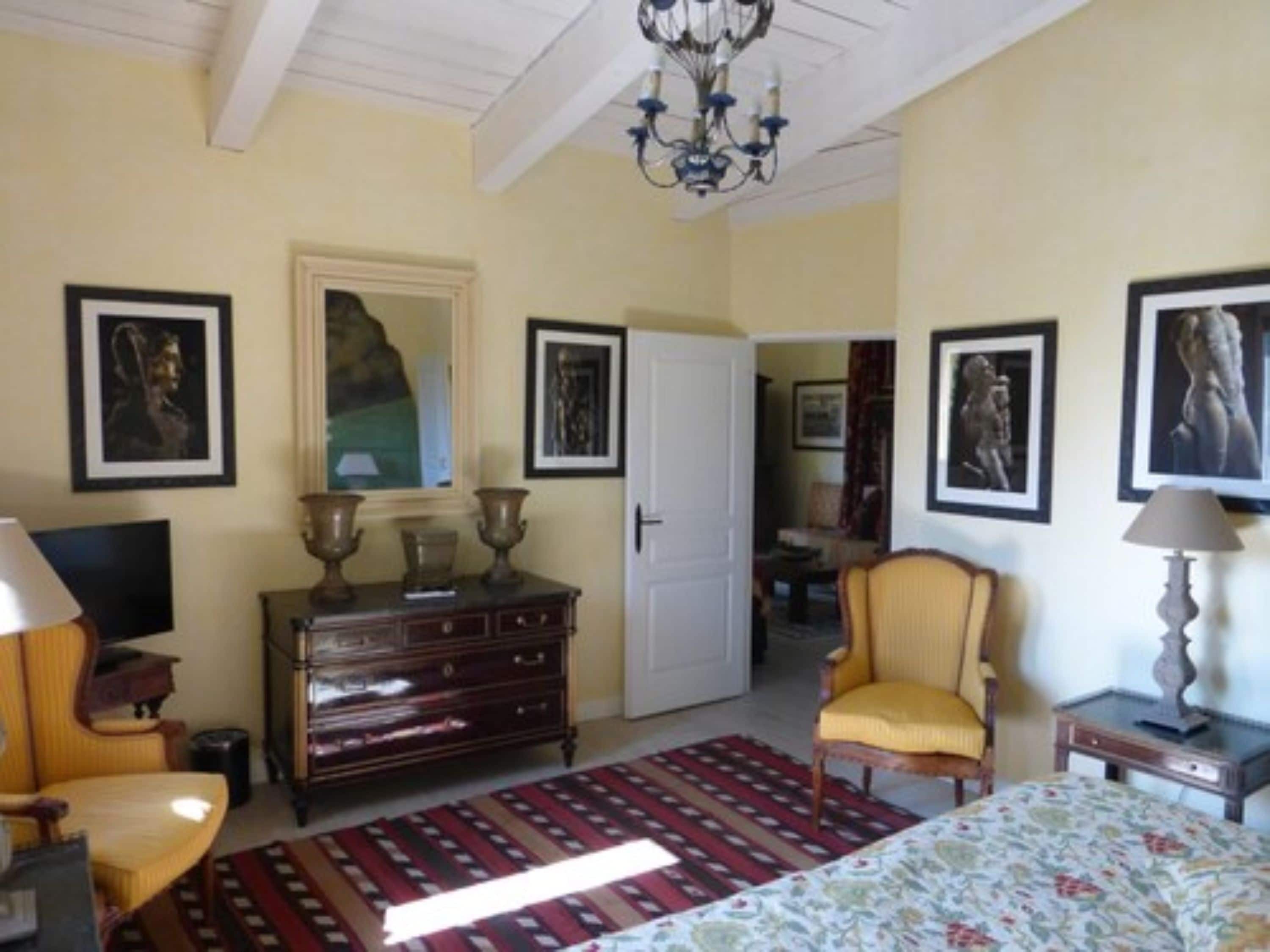 A bedroom with a bed, dresser, chair, lamp, and artwork on the walls.