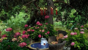 Een tuin met een tafel en stoelen, omringd door weelderig groen en roze bloemen.
