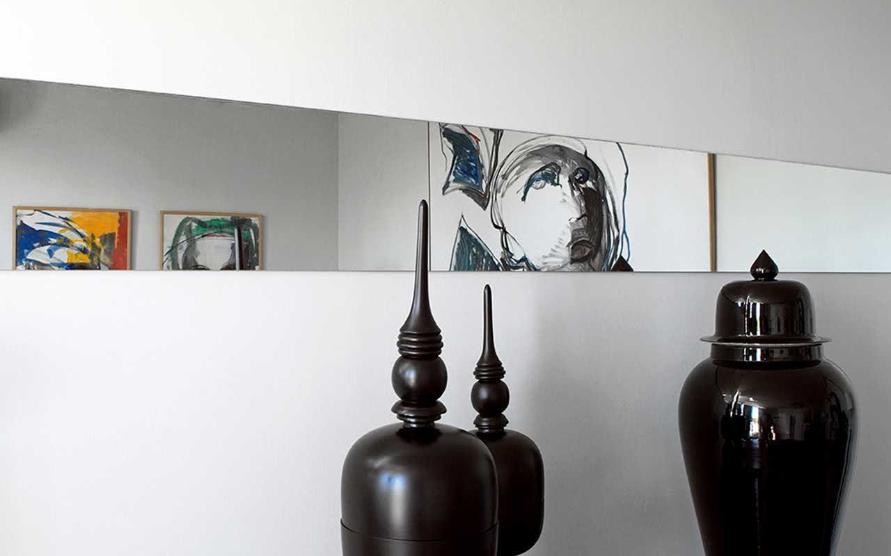 Une pièce avec un mur blanc, deux vases sombres et trois œuvres d’art encadrées.
