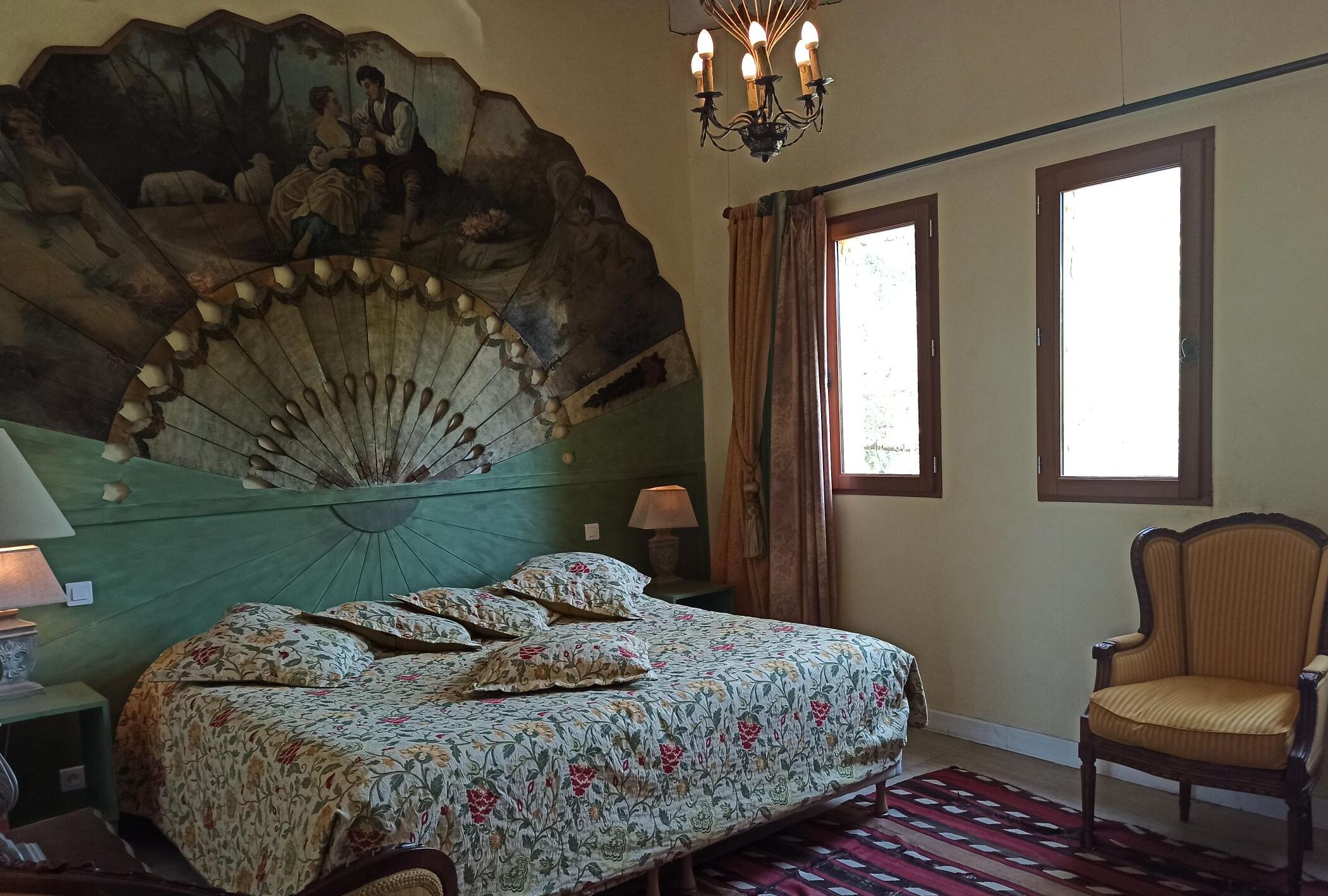 Una camera da letto con un letto, una sedia, un grande affresco e un lampadario.