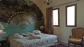 A bedroom with a bed, a chair, a large wall mural, and a chandelier.