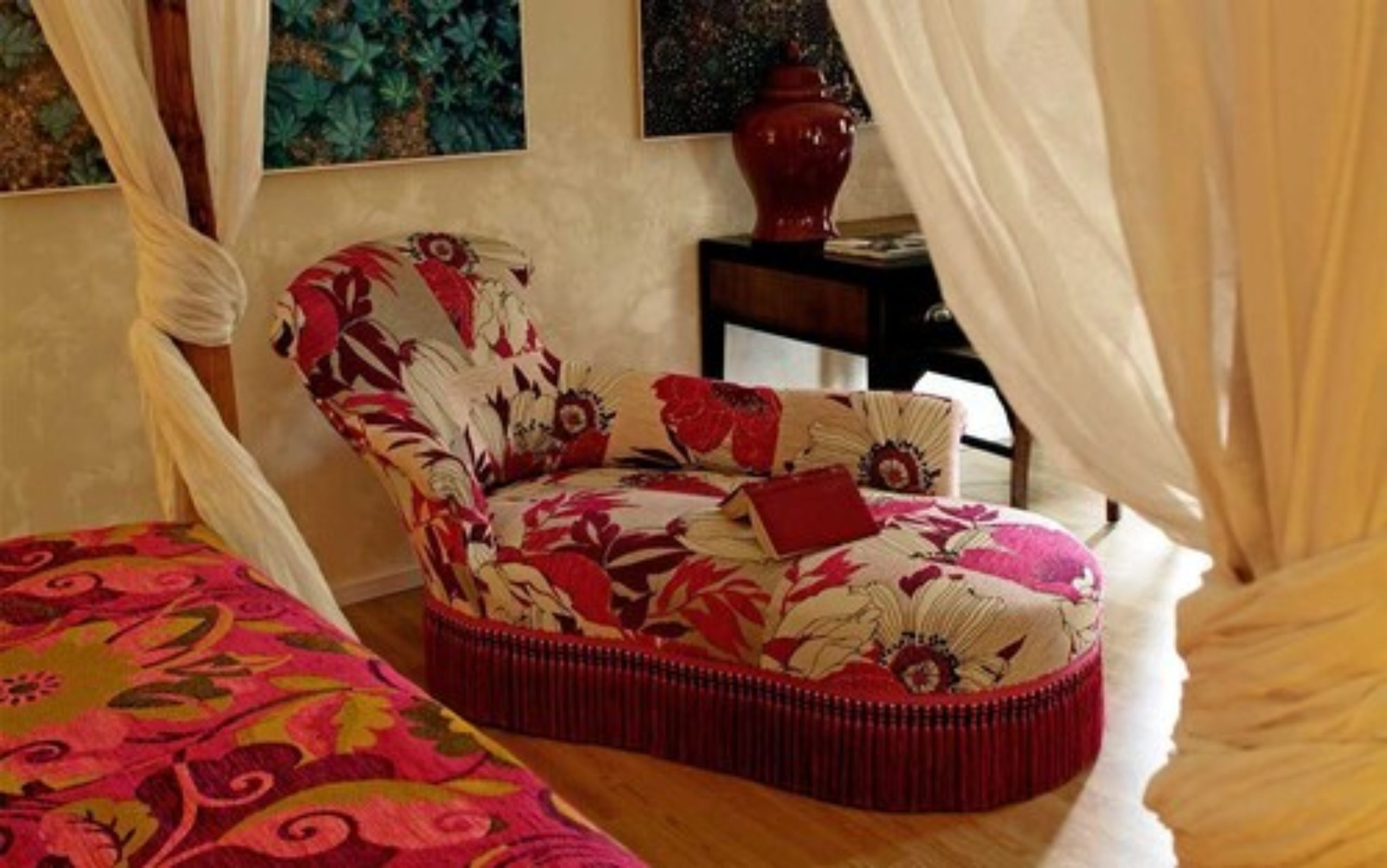 A bedroom with a floral-patterned chair, a bed with a colorful bedspread, and a vase on a nightstand.