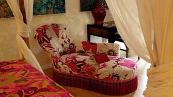 A bedroom with a floral-patterned chair, a bed with a colorful bedspread, and a vase on a nightstand.