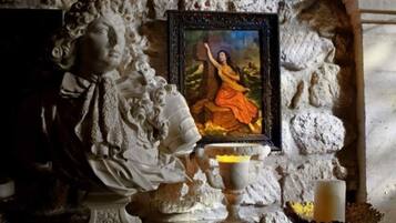 A statue of a robed figure with a framed painting of a woman in a red dress above it.