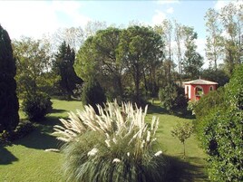 Un jardín con un edificio rojo, varios árboles y una zona verde.