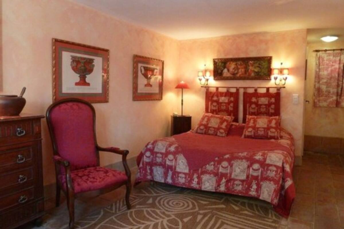 Une chambre à coucher avec un lit, une chaise, une commode et des tableaux encadrés accrochés au mur.