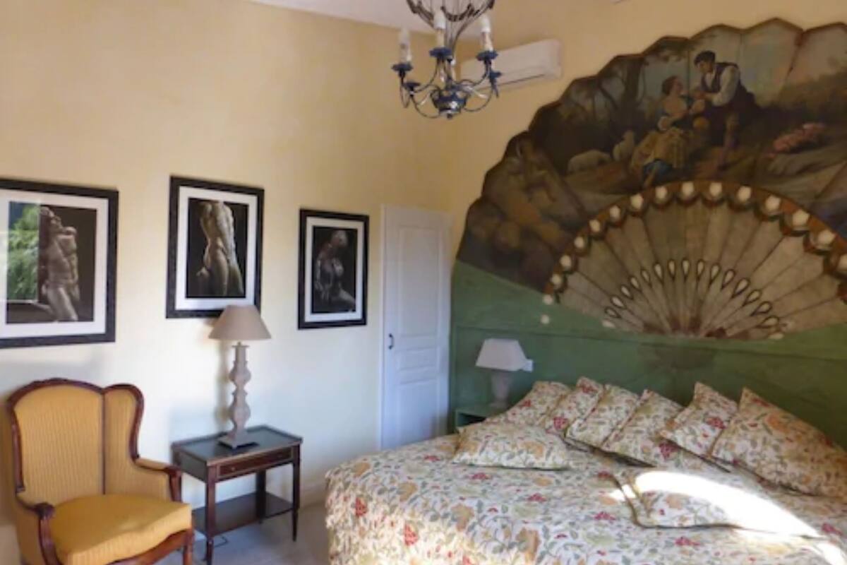 Une chambre à coucher avec un lit, une chaise, une lampe et trois tableaux encadrés accrochés au mur.