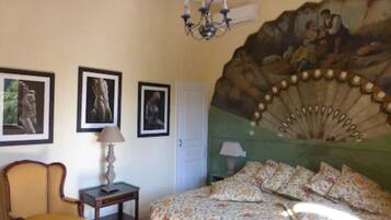 A bedroom with a bed, a chair, a lamp, and three framed pictures on the wall.