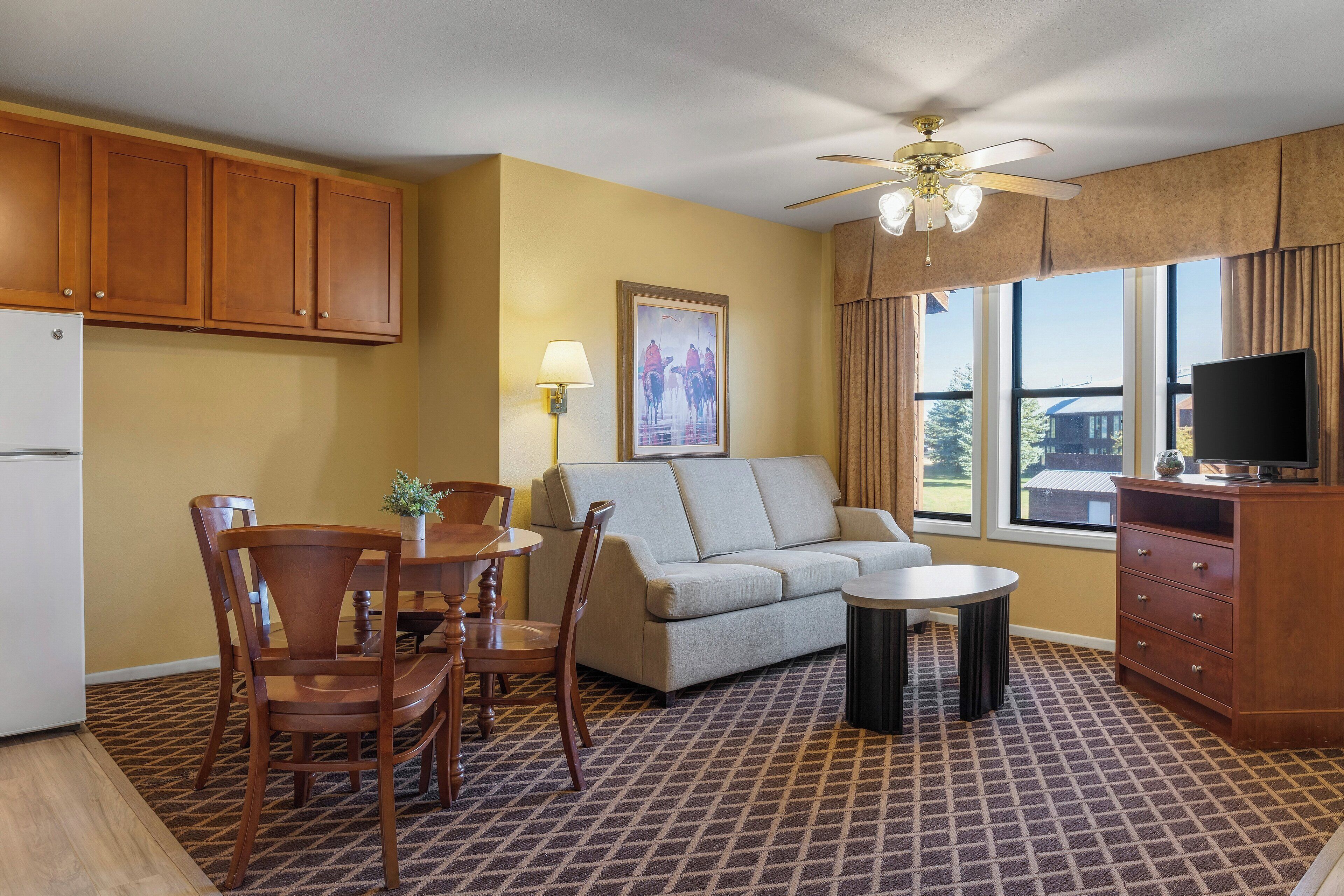 A compact living space with a kitchenette, a sofa, a dining table with chairs, a ceiling fan, and a television.
