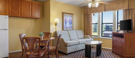 A compact living space with a kitchenette, a sofa, a dining table with chairs, a ceiling fan, and a television.