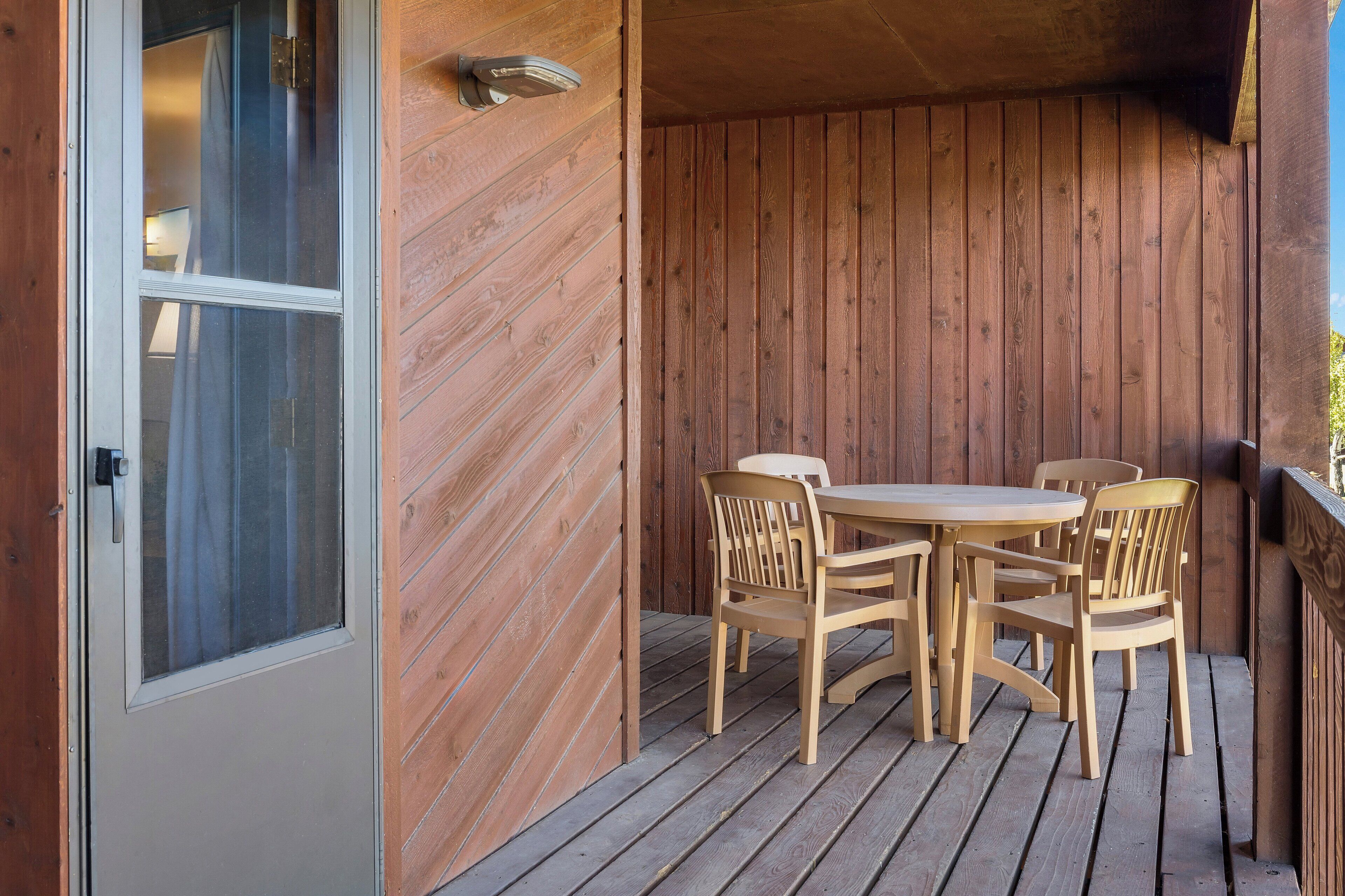 Una terraza de madera con una mesa, sillas, un ventanal corredero y una pared de madera.