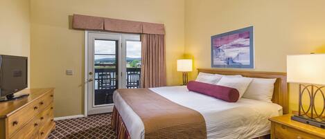 Une chambre d’hôtel avec un lit, un téléviseur posé sur une commode, une table de chevet avec une lampe, et une porte donnant sur un espace extérieur.