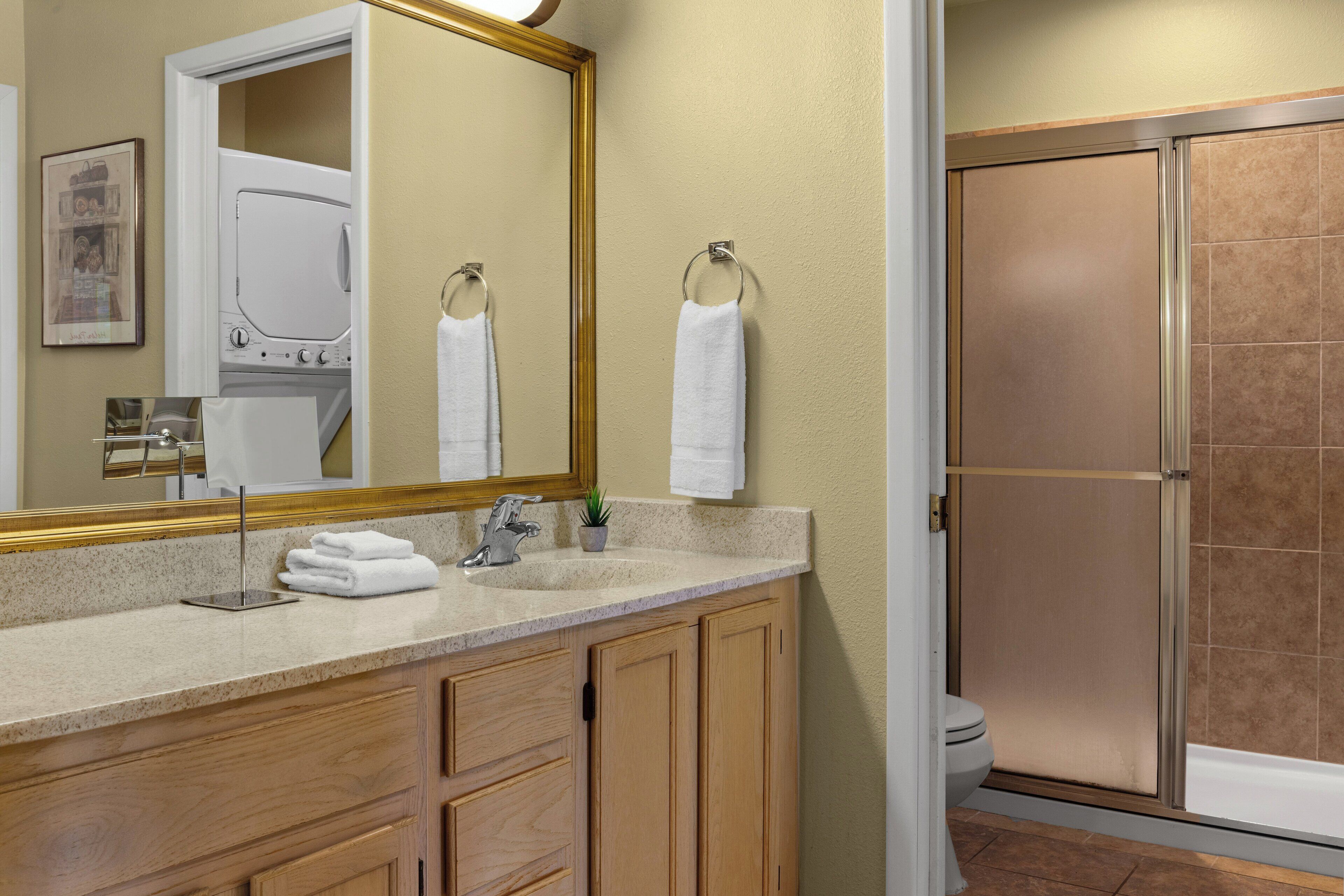 A bathroom with a wooden vanity, a large mirror, a towel rack, a shower enclosure, and a toilet.