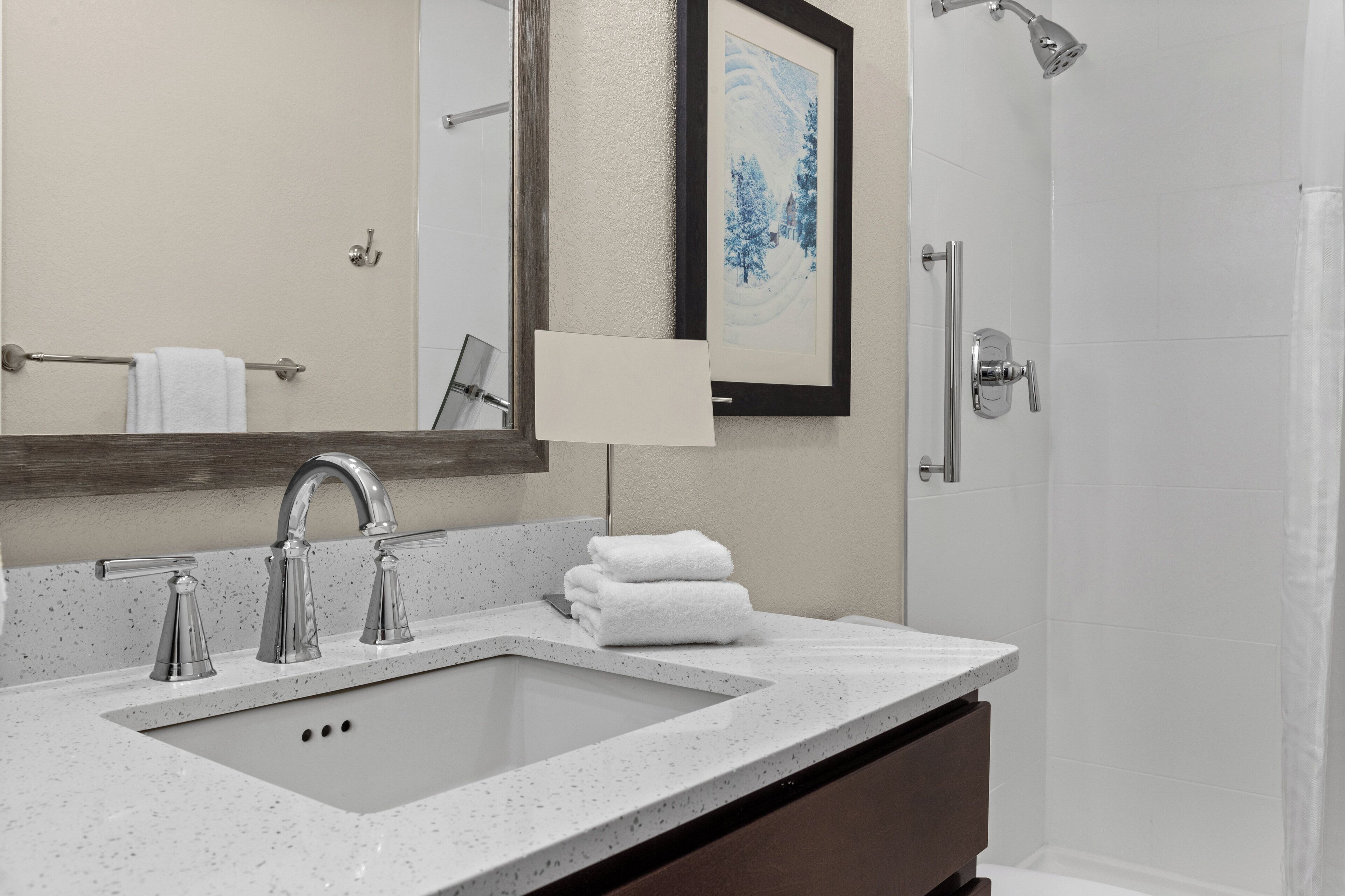 Une salle de bain équipée d’un lavabo, d’un miroir, d’une œuvre d’art encadrée et d’une douche.