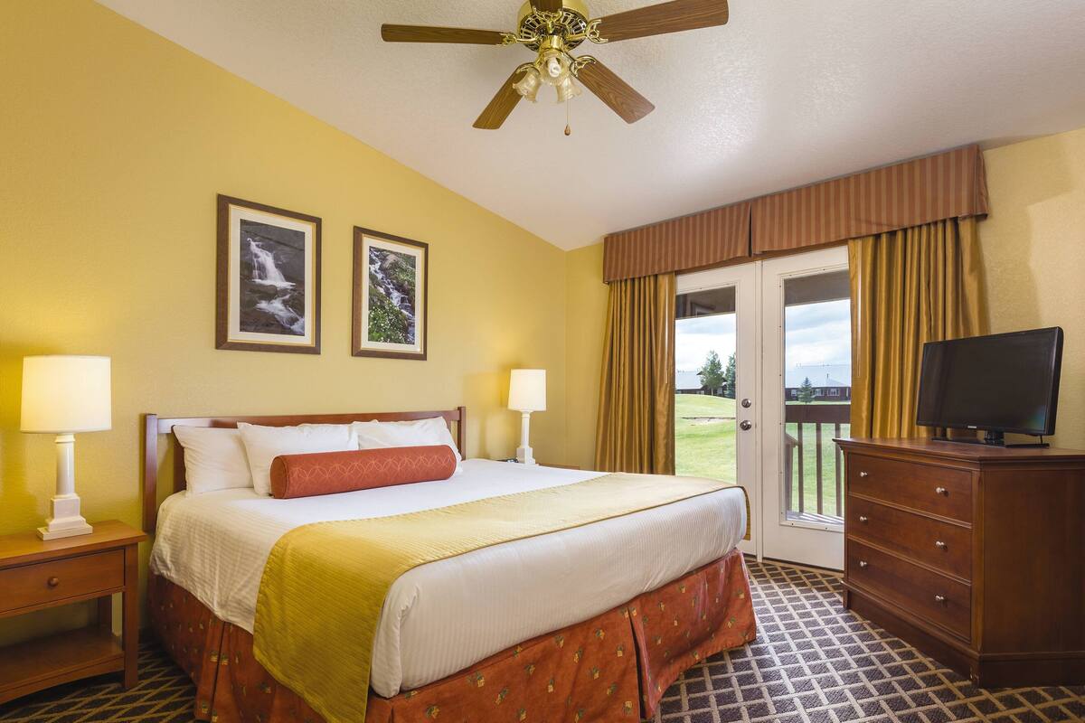 A hotel room with a bed, two bedside lamps, a television, a dresser, and a door leading to a balcony.