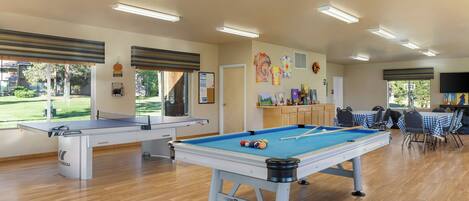 A pool table with a blue felt surface and a Playcraft logo, surrounded by chairs and tables with checkered tablecloths.