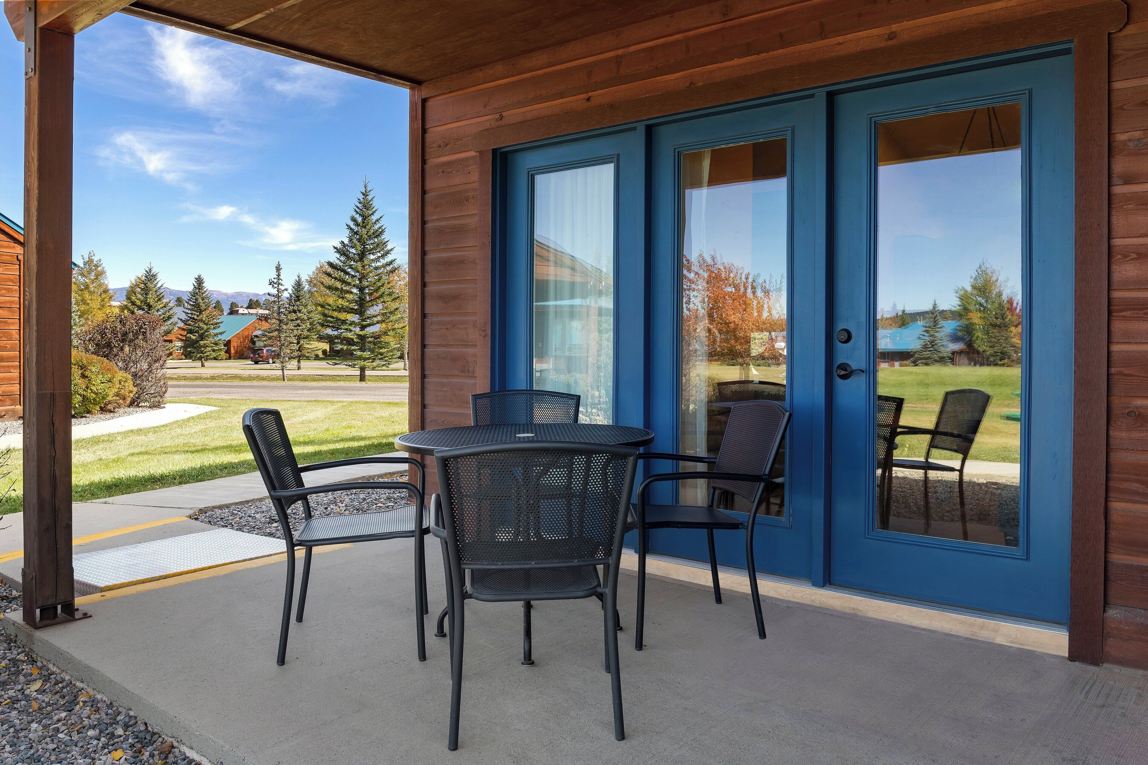 A covered patio with a table and chairs, a blue door, and a view of a mountain and trees.