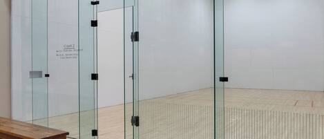 Una cancha de squash con paredes de vidrio, un banco de madera y un cartel que indica la cancha número 2 con normas específicas.