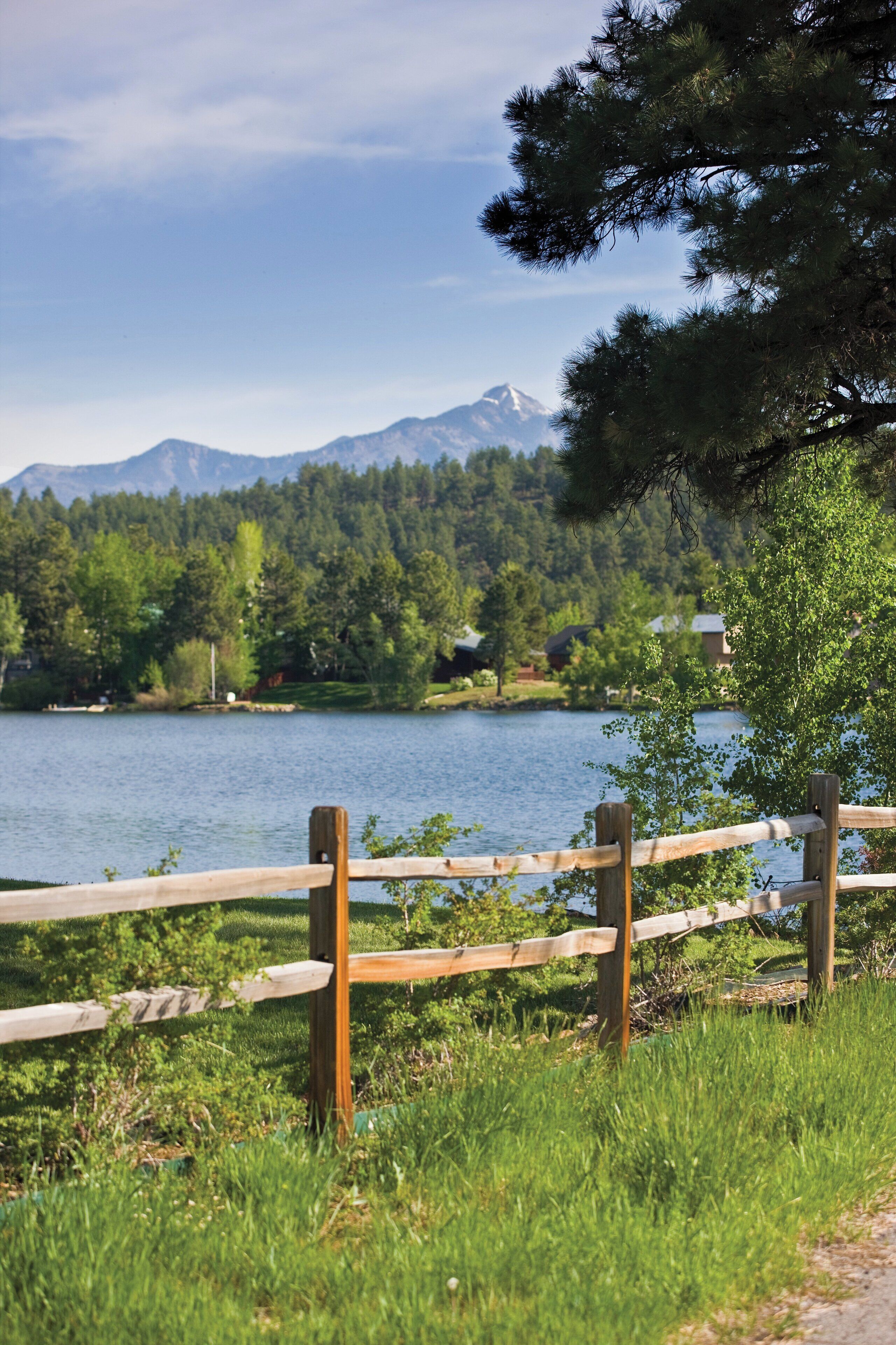 Una cerca de madera con vista a un lago y montañas al fondo.