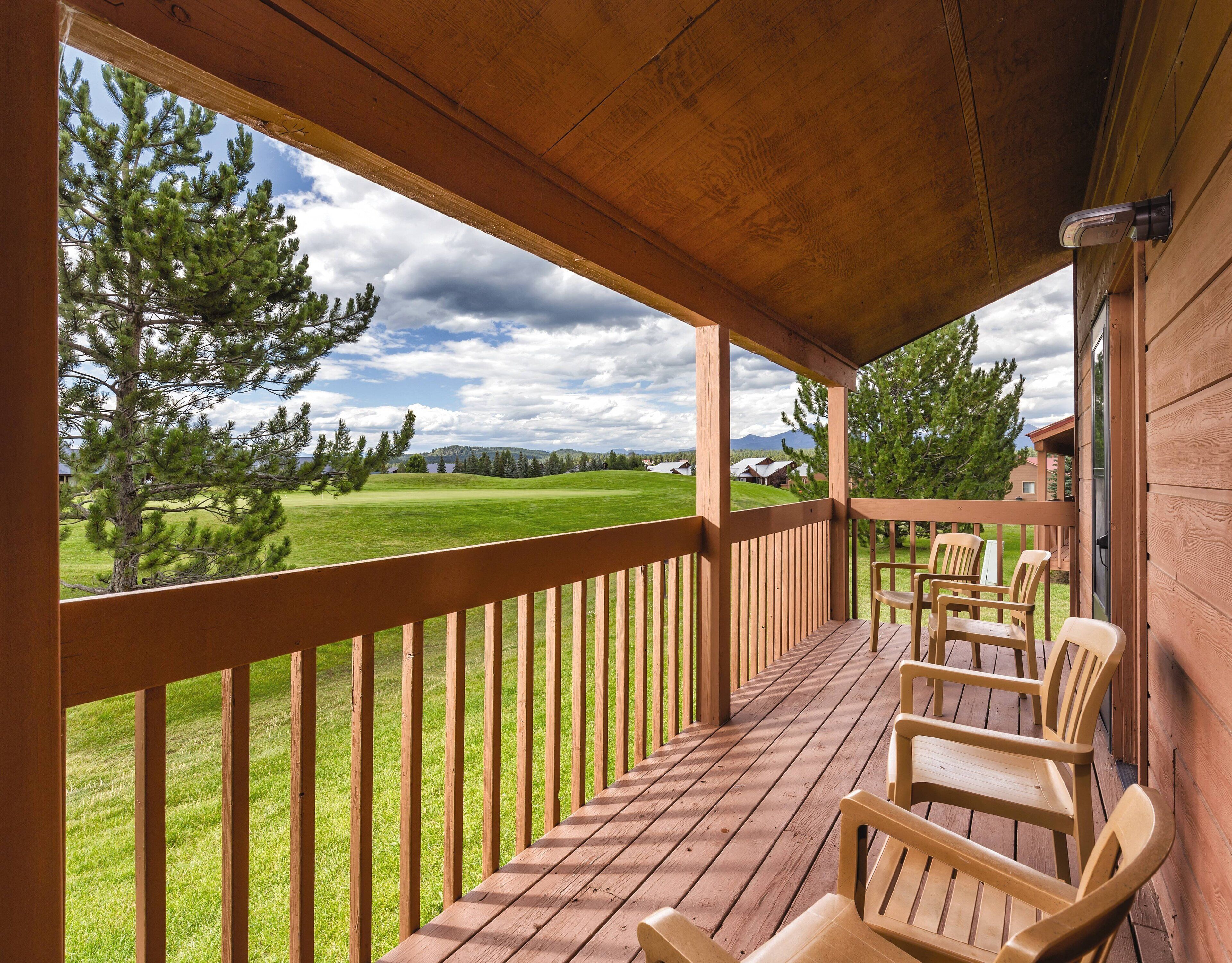 Un terrazza in legno con sedie, vista su un prato alberato e cielo nuvoloso.