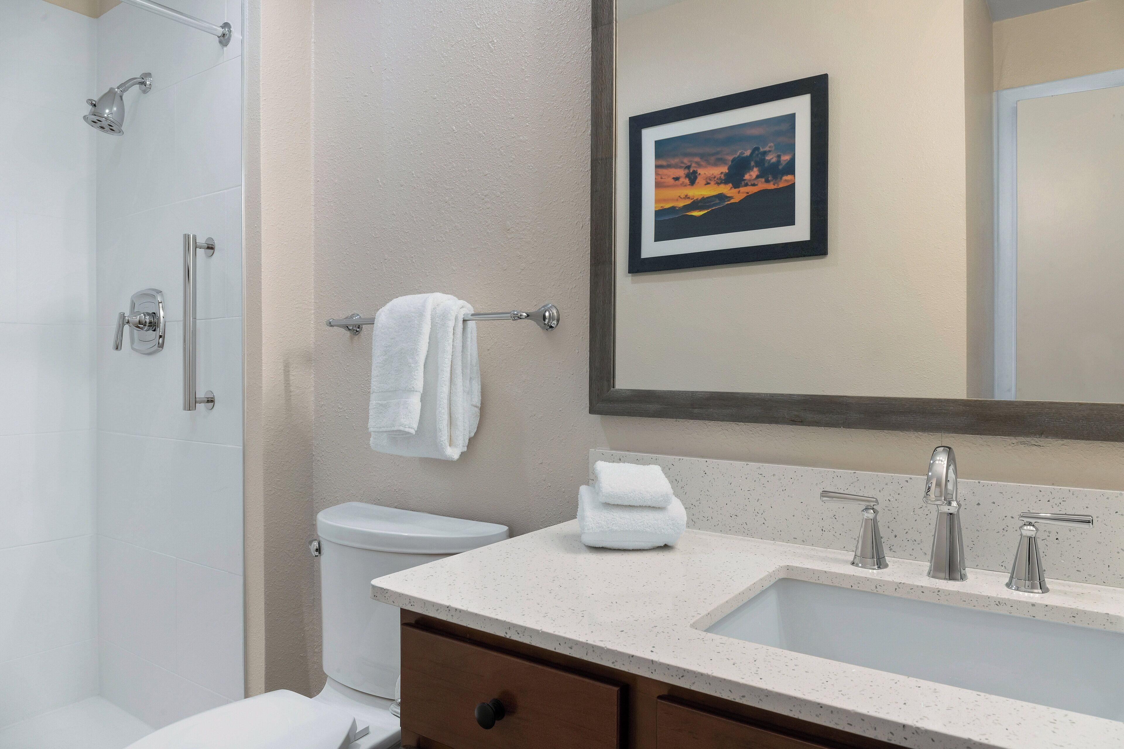 A bathroom with a shower, toilet, sink, and a framed picture on the wall.
