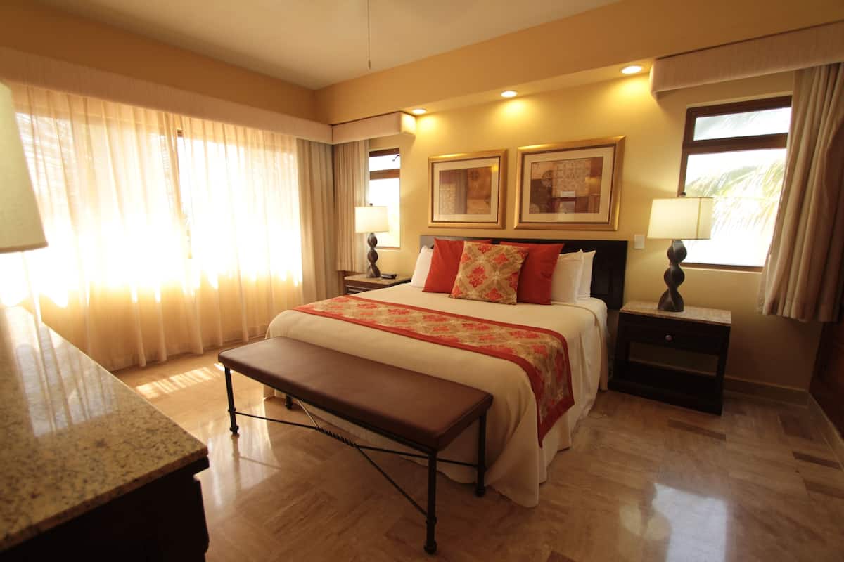A hotel room with a large bed, a bench, two bedside tables with lamps, and a window with curtains.