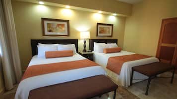 Een hotelkamer met twee bedden, elk voorzien van een bruine bank, witte beddengoed en oranje sierkussens. Er hangen kunstwerken in lijsten aan de muur en is een houten deur te zien.