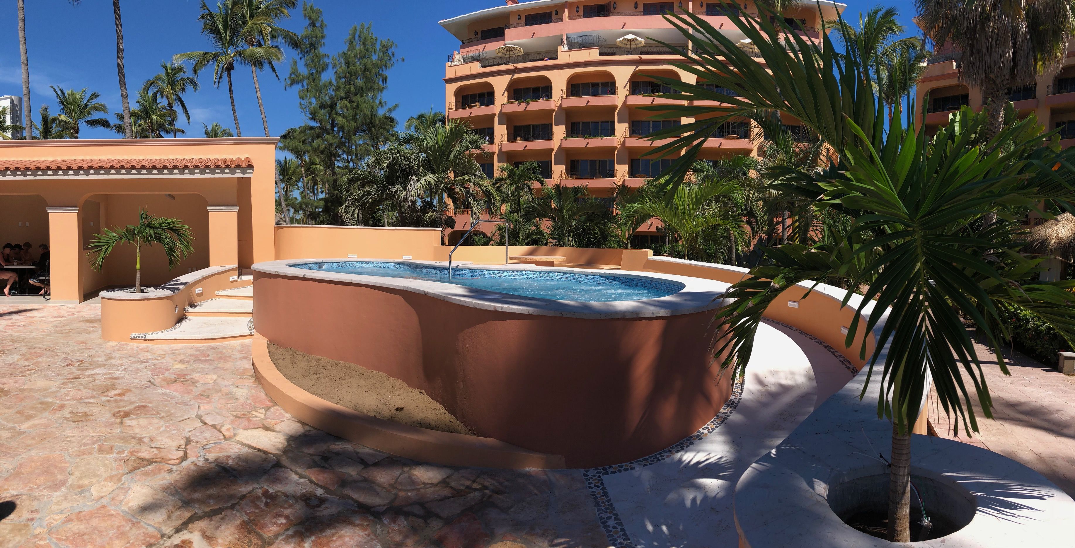 A hot tub surrounded by palm trees and a building with multiple balconies.