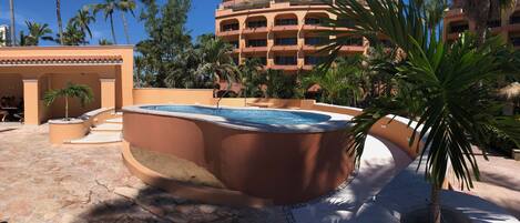 A hot tub surrounded by palm trees and a building with multiple balconies.