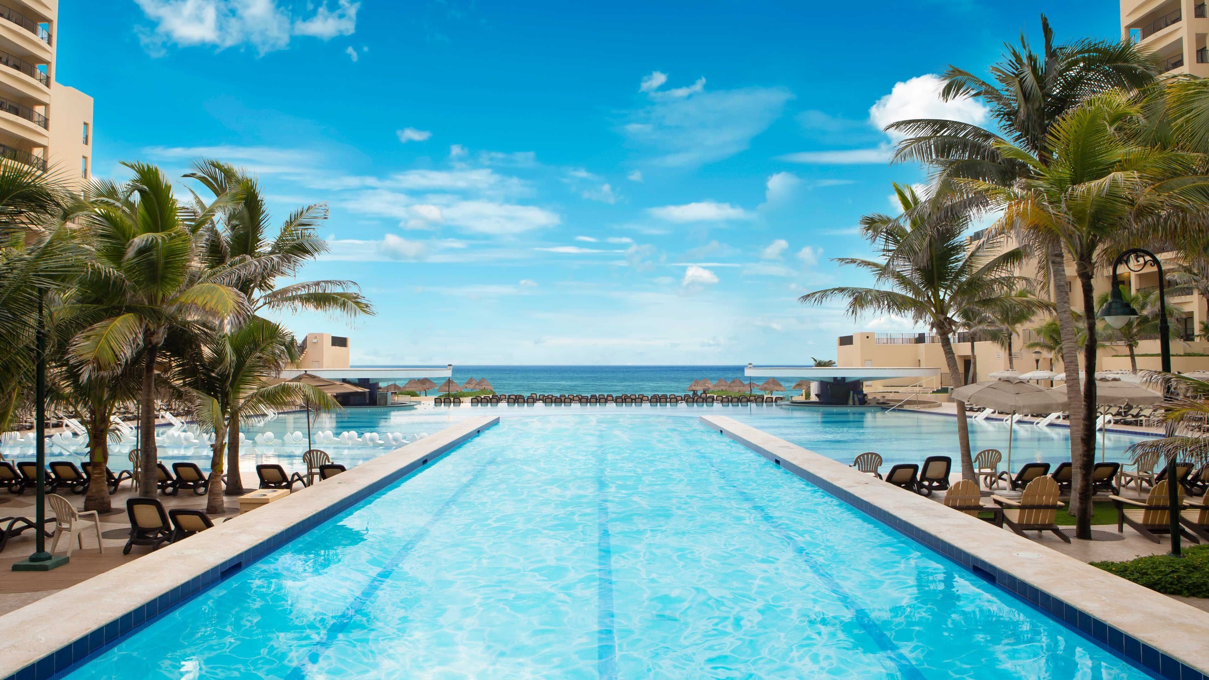 A pool with lounge chairs, palm trees, and a view of the ocean.