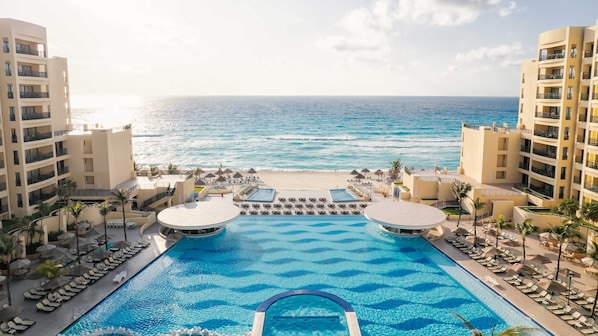 A resort pool with a view of the ocean, surrounded by palm trees and lounge chairs. - Holiday Inn Club Vacations The Royal Sands by IHG - All inclusive (Cancun)