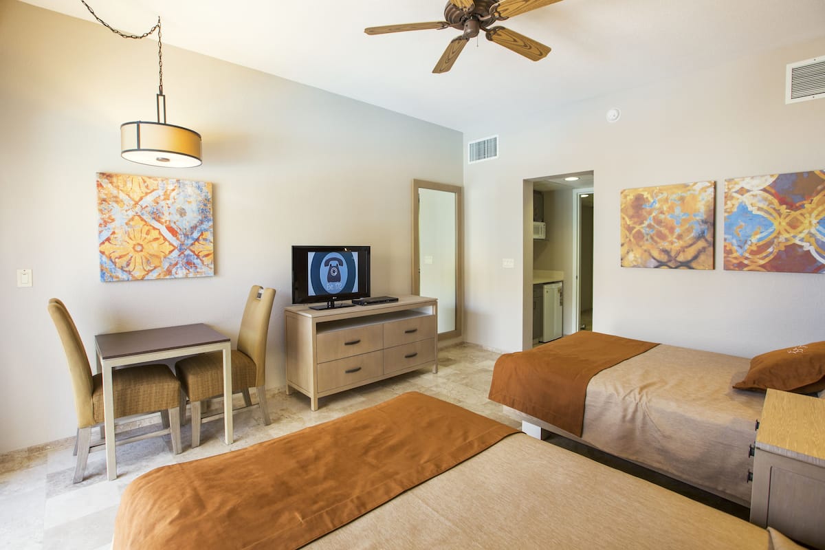 A hotel room with a bed, a desk with a chair, a television, and artwork on the walls.