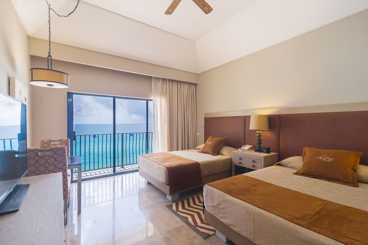 A hotel room with two beds, a desk, a chair, a nightstand, and a view of the ocean.