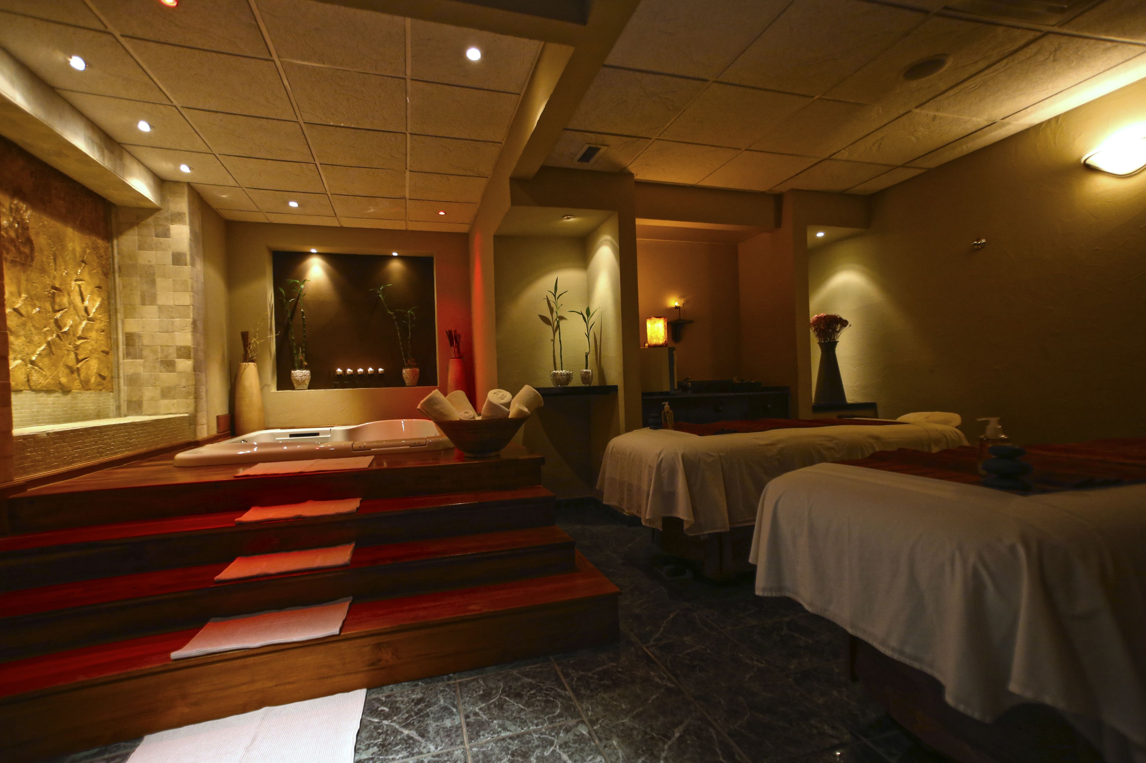 A spa room with a massage table, a hot tub, and a small seating area with steps.