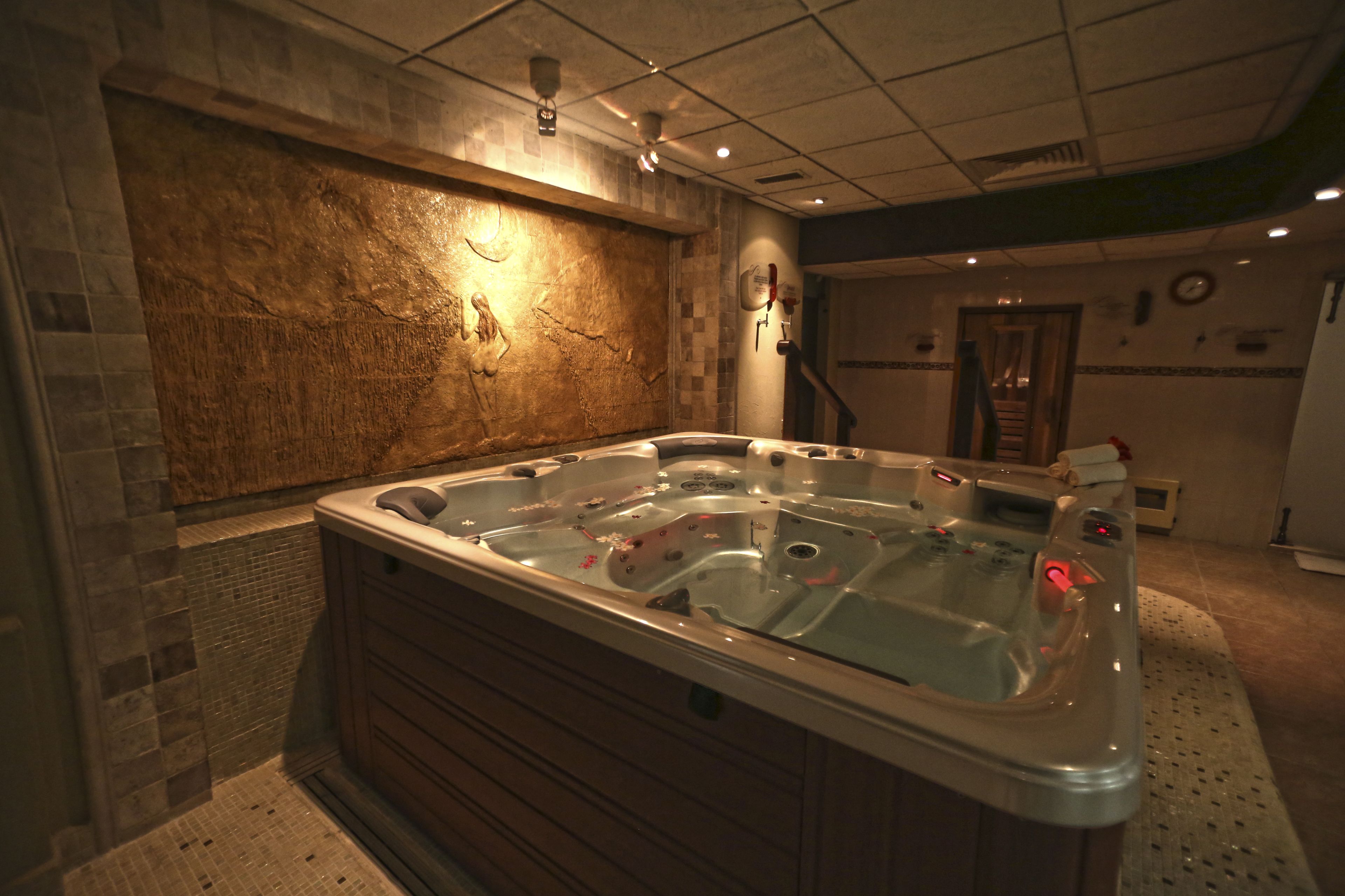 A hot tub in a room with stone walls and a tiled floor.