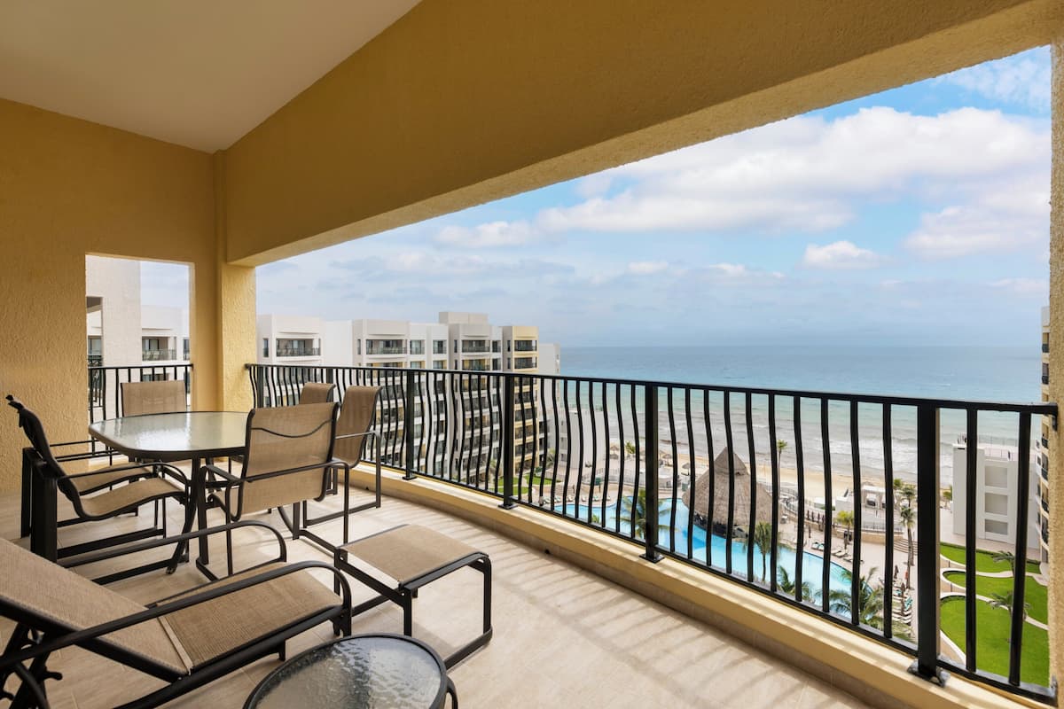 A balcony with a view of the ocean and a pool area.