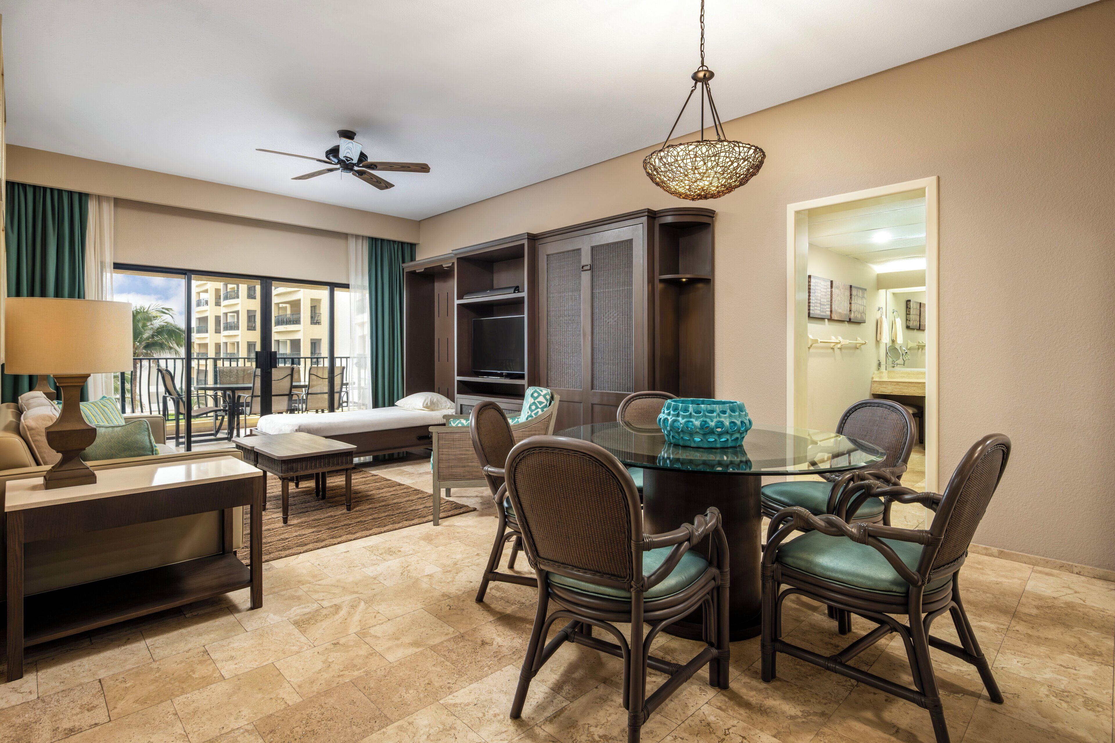 A hotel room with a dining area, a sofa, a TV, and a ceiling fan.