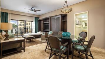 A hotel room with a dining area, a sofa, a TV, and a ceiling fan.