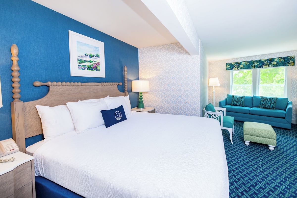 Habitación de hotel con una cama grande, pared azul, un cuadro enmarcado, sofá azul y alfombra estampada.