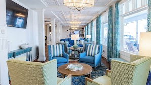 Un hall de hotel con muebles de tapicería azul y verde, una mesa de centro redonda y una araña.