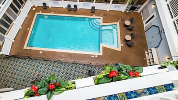 Una amplia piscina interior con solárium revestido, rodeada de barandillas blancas y amueblada con sillas y mesas.