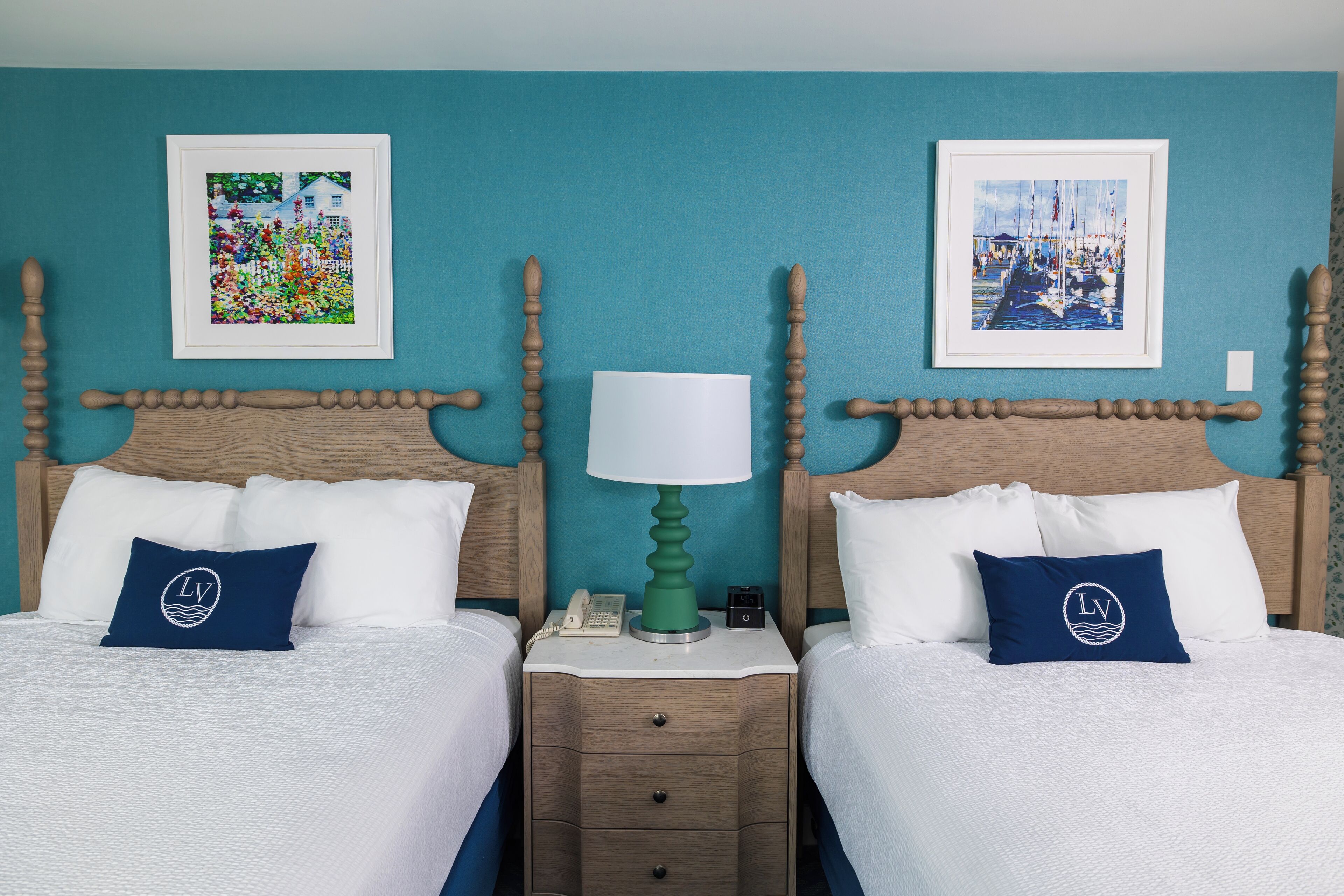 Habitación de hotel con dos camas, paredes verde azulado y obras de arte sobre cada cama.