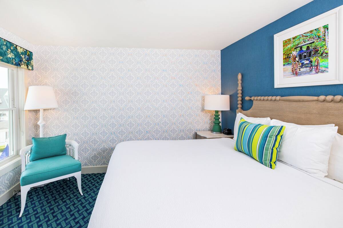 Un cuarto de hotel con una cama grande, una ventana con vistas, una silla y un cuadro en la pared.